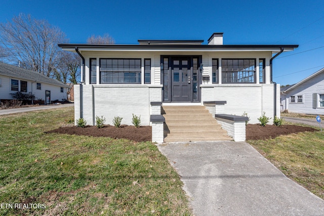 view of front of house featuring brick siding, a chimney, and a front yard