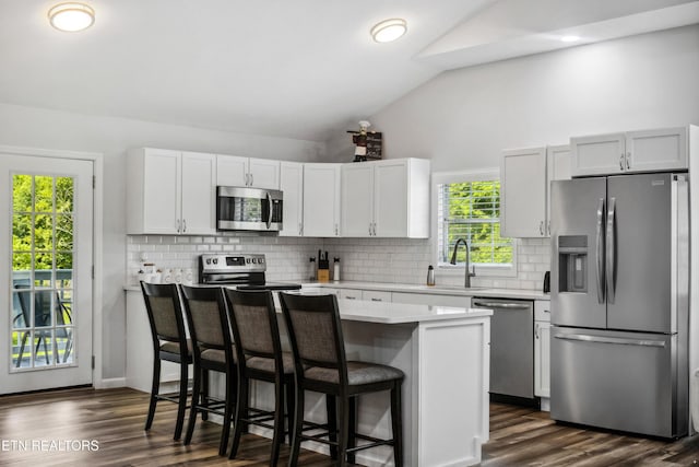 kitchen featuring a kitchen bar, sink, vaulted ceiling, stainless steel appliances, and white cabinets