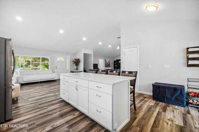 kitchen with stainless steel fridge, white cabinetry, a kitchen bar, dark hardwood / wood-style floors, and a kitchen island