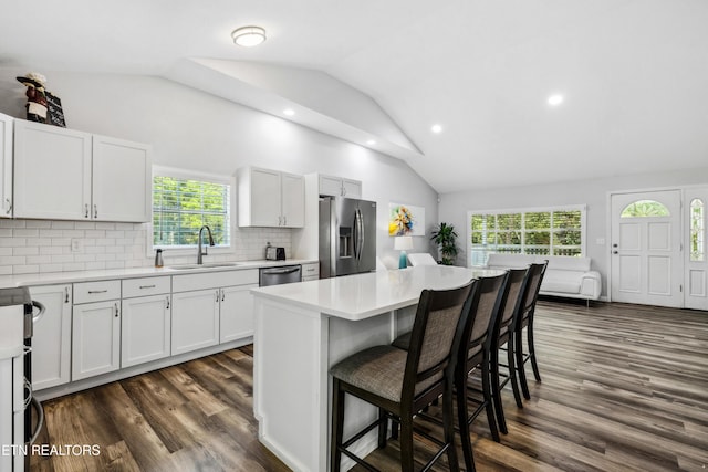 kitchen with lofted ceiling, sink, appliances with stainless steel finishes, white cabinetry, and decorative backsplash