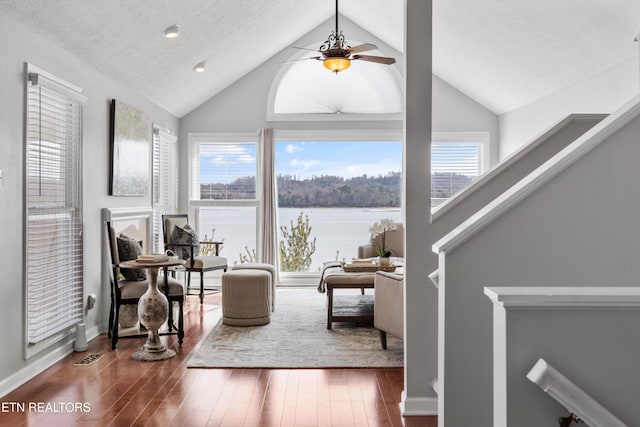 living area with baseboards, dark wood finished floors, a ceiling fan, a water view, and vaulted ceiling