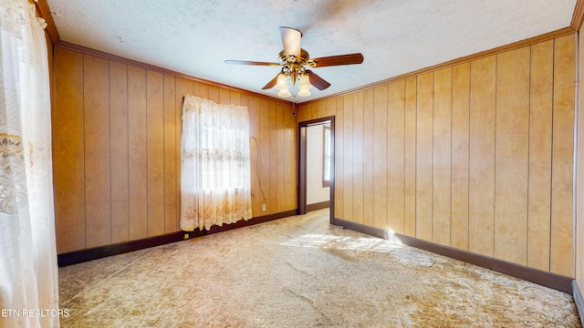 empty room with ceiling fan, wooden walls, ornamental molding, a textured ceiling, and light carpet