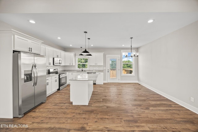 kitchen featuring appliances with stainless steel finishes, pendant lighting, white cabinetry, decorative backsplash, and a center island