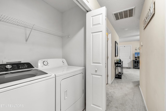 clothes washing area with light carpet, washer and dryer, and a textured ceiling