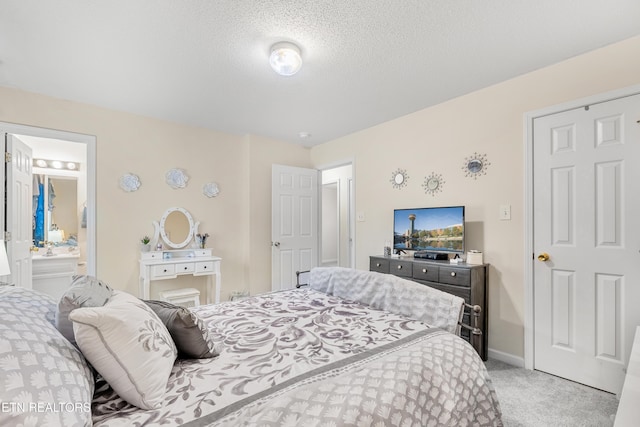 bedroom with ensuite bathroom, light carpet, and a textured ceiling