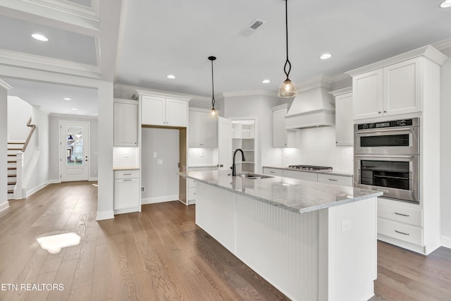 kitchen with sink, hanging light fixtures, light stone counters, white cabinets, and a center island with sink