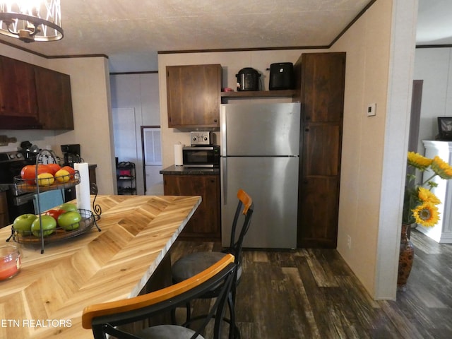 kitchen featuring dark wood-type flooring, dark brown cabinetry, an inviting chandelier, ornamental molding, and stainless steel fridge