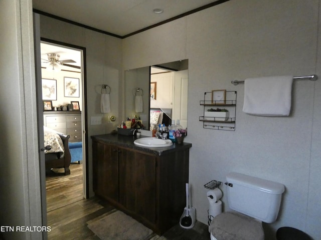 bathroom with toilet, wood-type flooring, ornamental molding, vanity, and ceiling fan