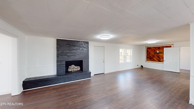 unfurnished living room with dark wood-type flooring and a brick fireplace