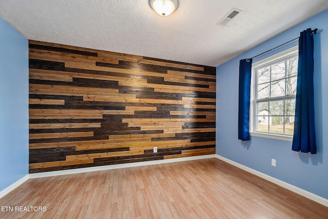 spare room featuring plenty of natural light, light wood-type flooring, a textured ceiling, and wood walls