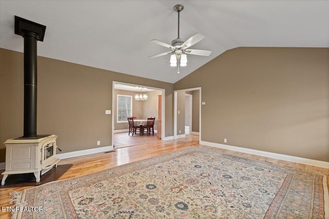 living room featuring lofted ceiling, ceiling fan with notable chandelier, wood-type flooring, and a wood stove