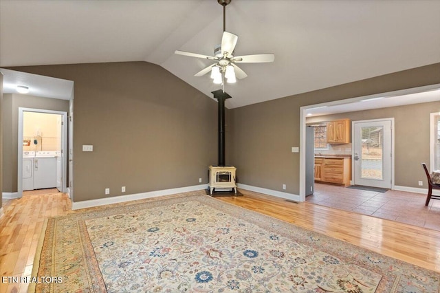 unfurnished living room with lofted ceiling, washer and dryer, a wood stove, and light wood-type flooring