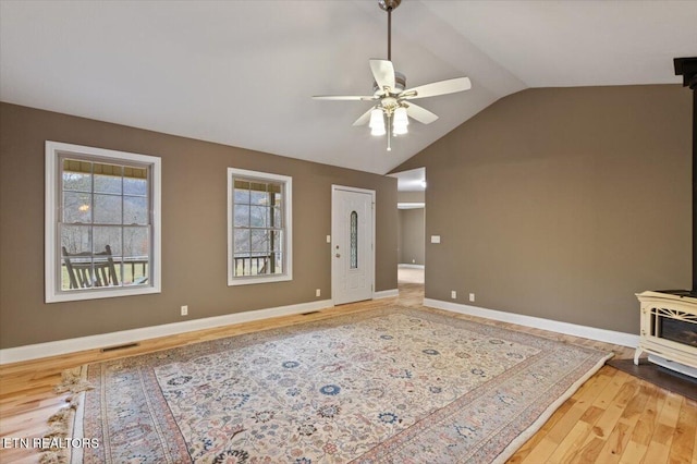 living room featuring lofted ceiling, hardwood / wood-style flooring, ceiling fan, and a wood stove