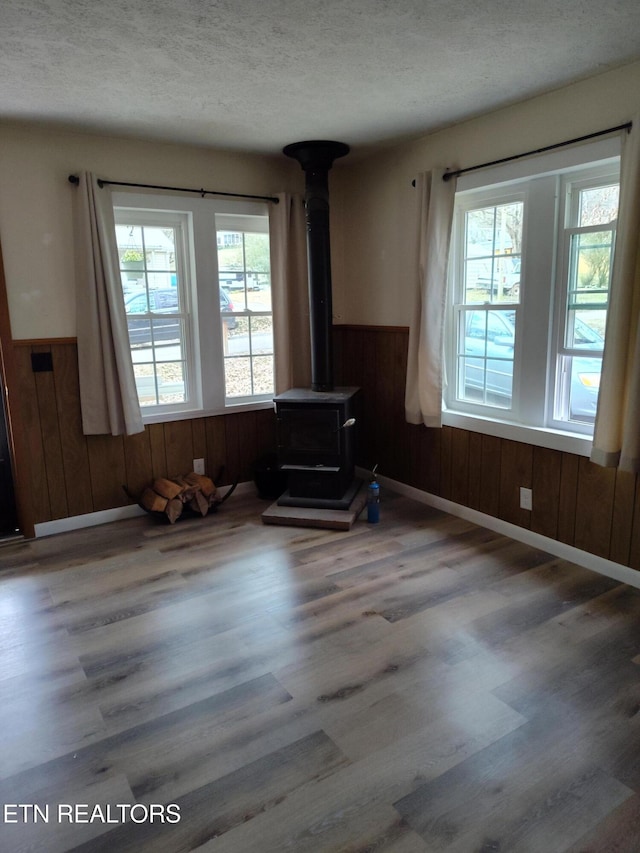 unfurnished living room with a wood stove, hardwood / wood-style floors, a textured ceiling, and wood walls