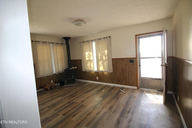 entryway featuring a wood stove, wooden walls, wood finished floors, and wainscoting