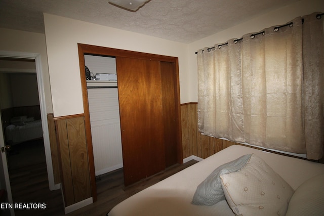 bedroom with a wainscoted wall, a closet, a textured ceiling, and wood walls