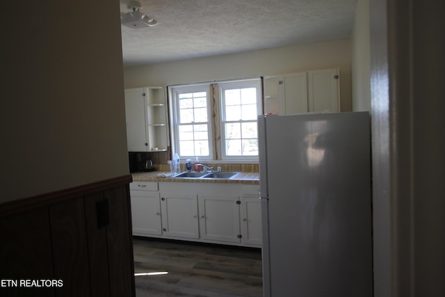 kitchen featuring a textured ceiling, white cabinets, a sink, and freestanding refrigerator