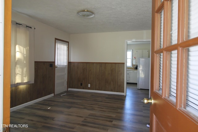 empty room with dark wood-style floors, a wainscoted wall, wood walls, and a textured ceiling