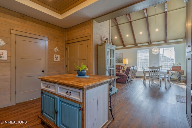 kitchen with decorative light fixtures, wooden walls, lofted ceiling with beams, and a center island