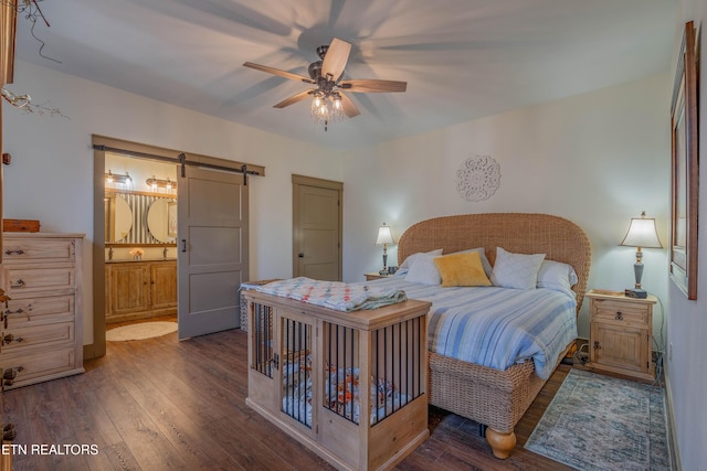 bedroom featuring a barn door, dark hardwood / wood-style floors, ceiling fan, and ensuite bath