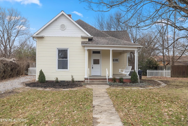 view of front of home with a porch, a front lawn, a shingled roof, and fence