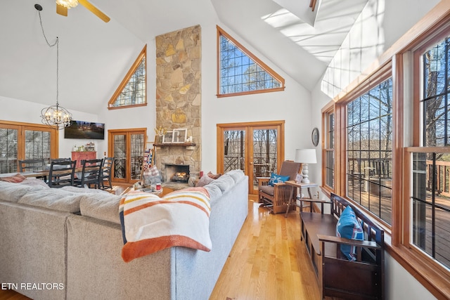 living room featuring light hardwood / wood-style flooring, high vaulted ceiling, a notable chandelier, a fireplace, and french doors