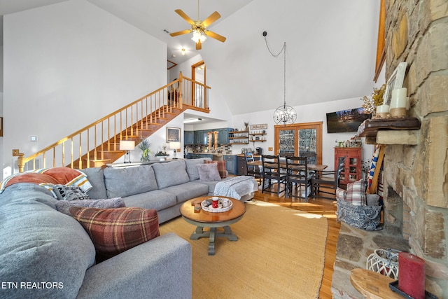 living room with ceiling fan with notable chandelier, high vaulted ceiling, and light hardwood / wood-style flooring