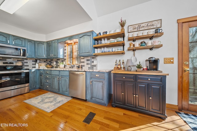 kitchen featuring tasteful backsplash, appliances with stainless steel finishes, blue cabinets, and light wood-type flooring