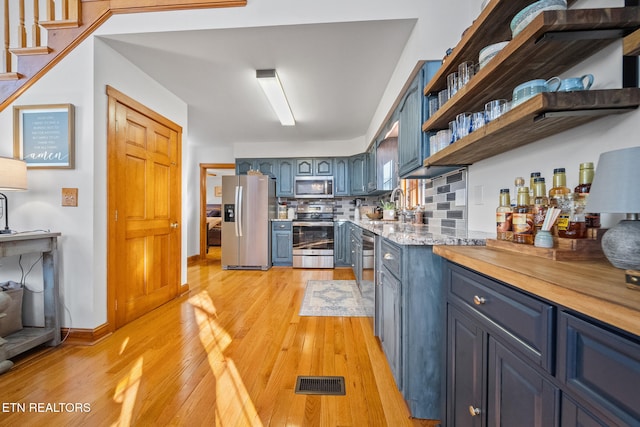 kitchen featuring appliances with stainless steel finishes, sink, backsplash, blue cabinetry, and light hardwood / wood-style flooring