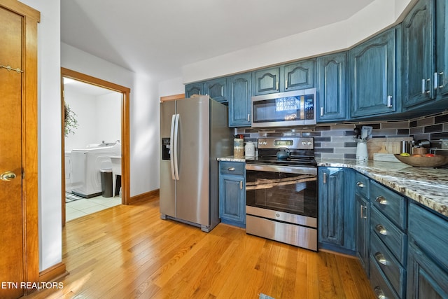 kitchen with appliances with stainless steel finishes, decorative backsplash, light hardwood / wood-style floors, light stone counters, and washer and clothes dryer