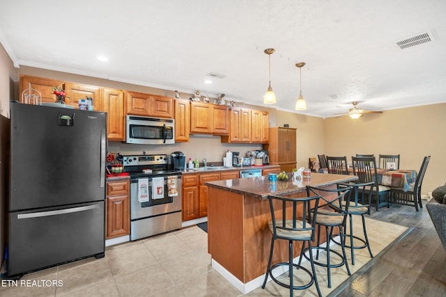 kitchen featuring crown molding, decorative light fixtures, a kitchen breakfast bar, a kitchen island, and stainless steel appliances