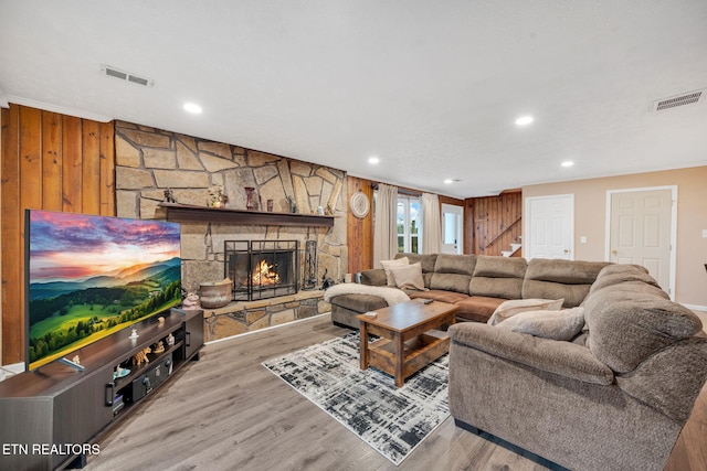 living room featuring a stone fireplace, light hardwood / wood-style floors, and wood walls