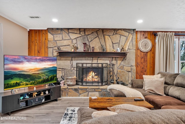 living room featuring hardwood / wood-style flooring, wooden walls, ornamental molding, and a stone fireplace