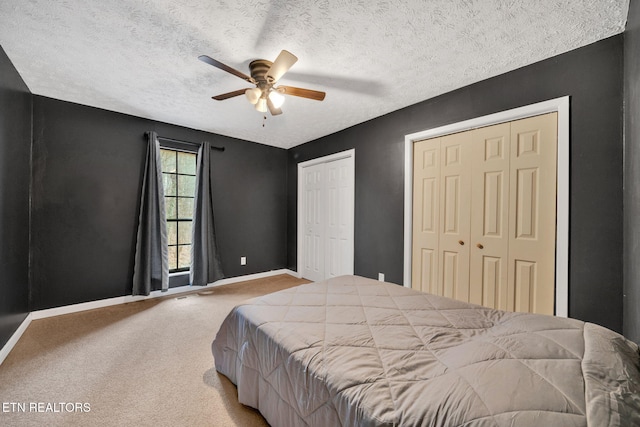 bedroom with ceiling fan, light colored carpet, a textured ceiling, and two closets