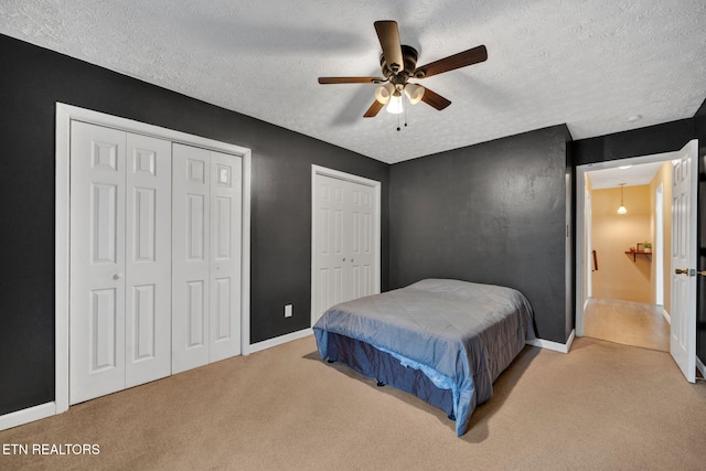 bedroom with multiple closets, ceiling fan, light carpet, and a textured ceiling