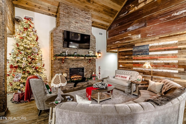 living room featuring wood ceiling, hardwood / wood-style flooring, high vaulted ceiling, a stone fireplace, and wood walls