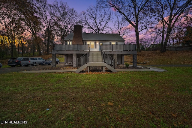 back house at dusk with a wooden deck and a lawn