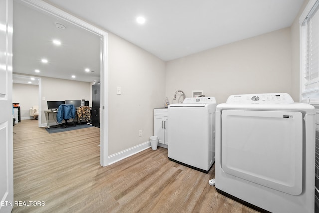 laundry area with light hardwood / wood-style floors, washing machine and dryer, and cabinets