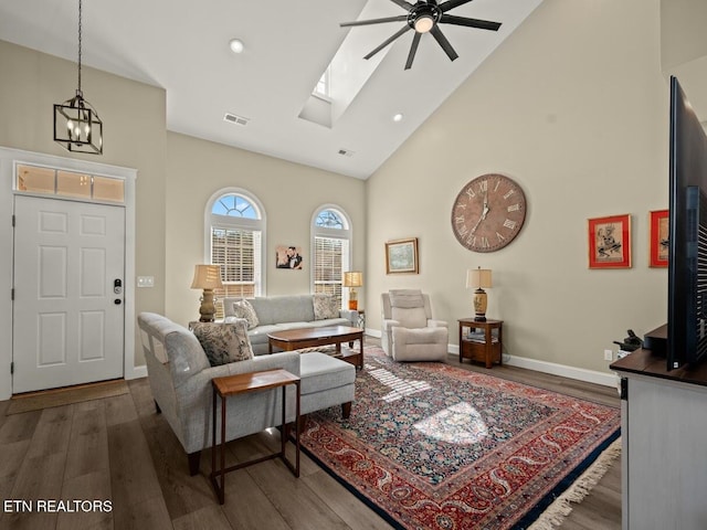 living room featuring ceiling fan with notable chandelier, hardwood / wood-style floors, high vaulted ceiling, and a skylight