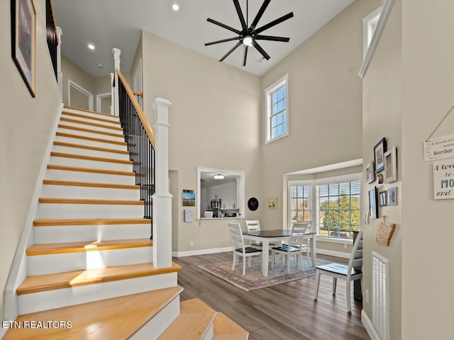 staircase with wood-type flooring, ceiling fan, and a high ceiling