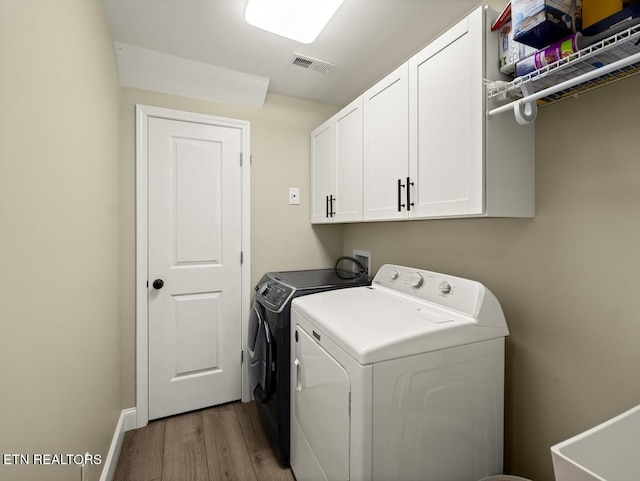 laundry area featuring sink, wood-type flooring, washing machine and dryer, and cabinets