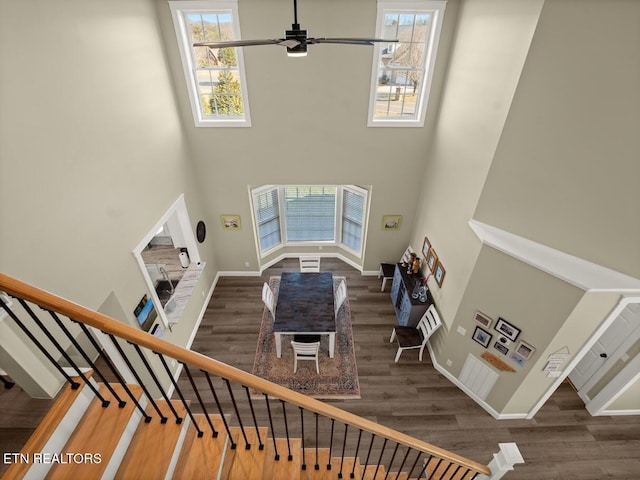 staircase with ceiling fan, a towering ceiling, wood-type flooring, and a healthy amount of sunlight