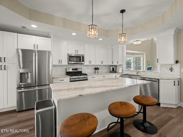 kitchen with sink, white cabinetry, stainless steel appliances, a kitchen island, and decorative light fixtures