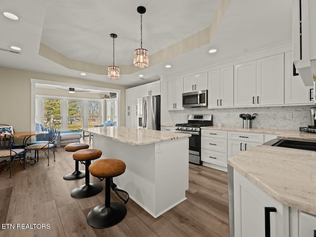 kitchen featuring stainless steel appliances, a raised ceiling, hanging light fixtures, and white cabinetry