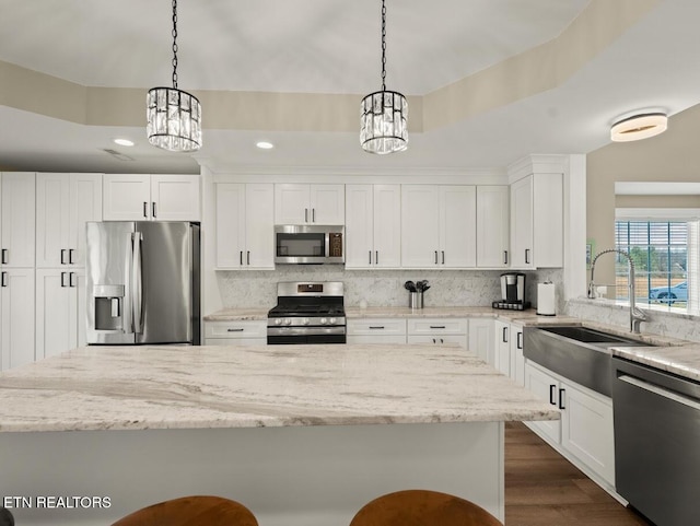 kitchen featuring appliances with stainless steel finishes, light stone countertops, hanging light fixtures, and white cabinets