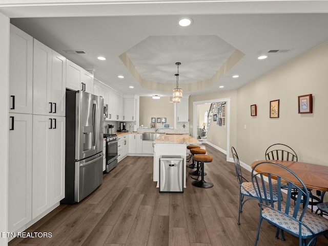 kitchen featuring appliances with stainless steel finishes, a kitchen breakfast bar, a raised ceiling, pendant lighting, and white cabinets