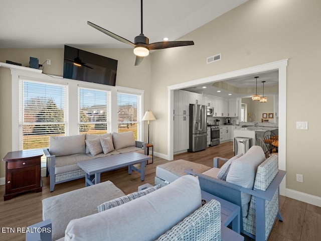 living room featuring ceiling fan with notable chandelier, wood-type flooring, and high vaulted ceiling