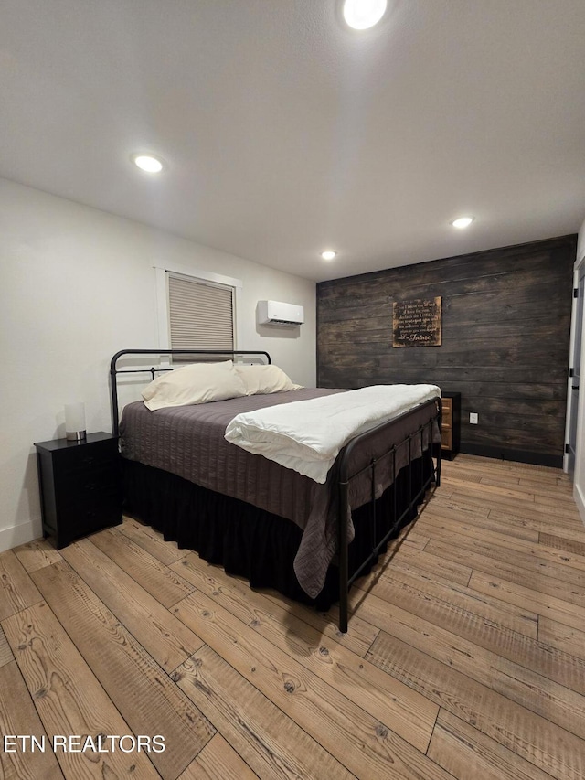 bedroom featuring wood walls, a wall mounted air conditioner, and light wood-type flooring