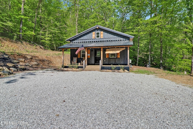 view of front facade featuring a porch, gravel driveway, and a forest view