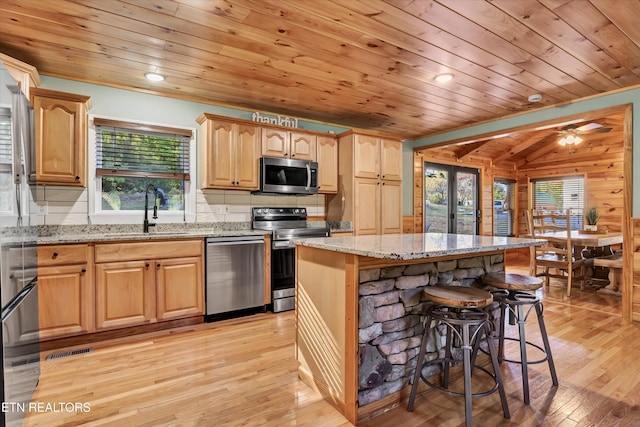 kitchen with a kitchen bar, sink, light stone counters, a kitchen island, and stainless steel appliances